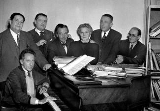 Spectacle musical réalisé par le Trio Manitra Image en noir et blanc de six hommes et une femme au bord d'un piano
